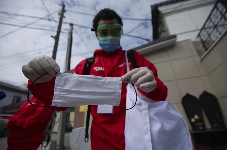 На фото - волонтер раздает многоразовые защитные маски горожанам