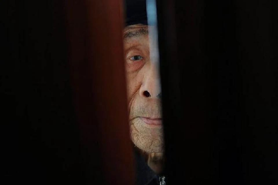 Старик смотрит в щель приоткрытой двери в китайском доме для престарелых