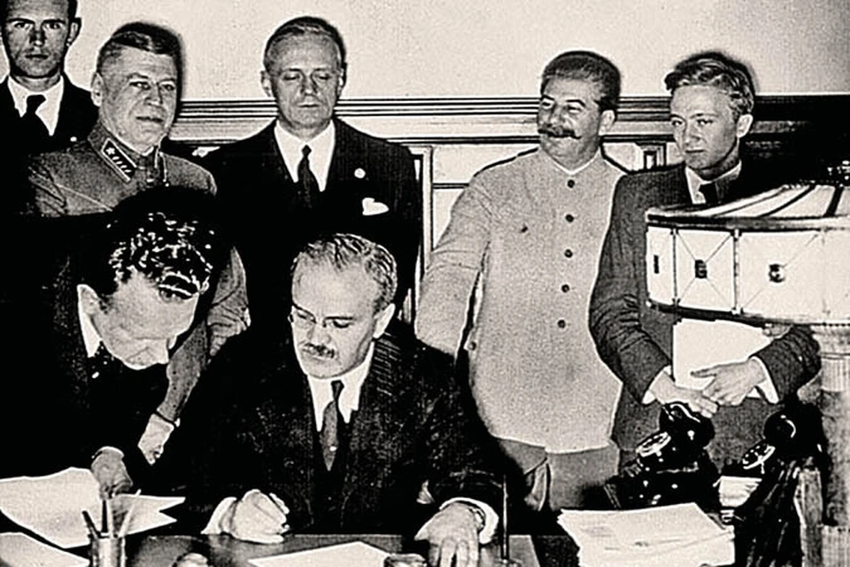 Молотов подписывает пакт, прямо за его спиной Риббентроп, справа от которого - Сталин.